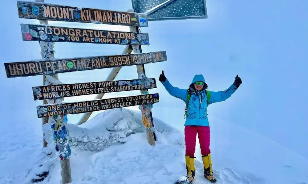 Ein Kletterer feiert vor dem Uhuru-Peak-Gipfelschild